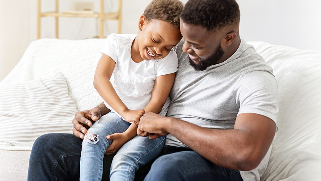A young boy sits on his father's lap and give him a fist bump.